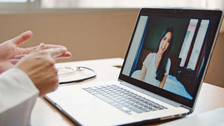 Doctor online video call explain treatment, symptom check with Asian patient woman connecting from home, using laptop computer in hospital office. Telemedical, Covid-19 new normal healthcare conceptの写真素材