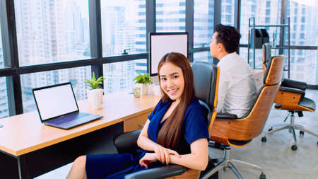 Portrait of happy Asian businesswoman sit and smile in startup company office, business coworker working on desktop and laptop computer. Corporate office, small business, or teamwork conceptの写真素材