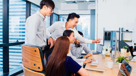 Group of Asian business people work together in team brainstorm discussion on desktop computer in office. Corporate business, coworker teamwork, or financial consultant meeting conceptの写真素材