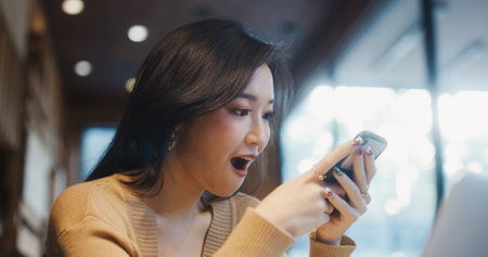 Beautiful young Asian woman use smartphone in coffee shop, happy surprise smiling. People modern lifestyle, internet communication technology, or online shopping conceptの写真素材