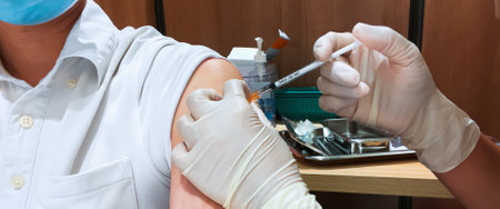 Asian man wear face mask receive Coronavirus vaccine injection jab by nurse or general practitioner at hospital or healthcare clinic service. People on vaccination or Covid-19 pandemic relief conceptの写真素材