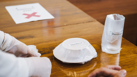 Close-up restaurant waitress serving sanitized dish, spoon and fork to Asian male customer. Business...