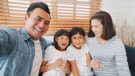 Young happy Asian family talk to selfie point of view camera, online remote video call with friend. Internet information technology, social distancing, or coronavirus new normal lifestyle conceptの写真素材