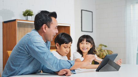 Asian father teach young son and daughter homework, using digital tablet at home. E-learning lifestyle, happy family homeschooling, children remote distance education, or internet technology conceptの写真素材