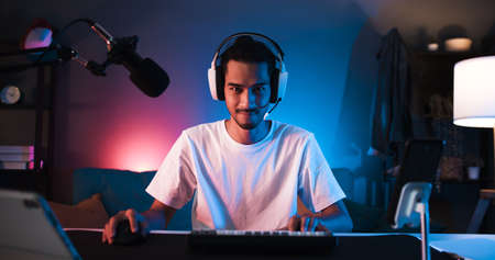 Young confident Asian man playing online computer video game, colorful lighting broadcast streaming live at home. Gamer lifestyle, E-Sport online gaming technology conceptの写真素材