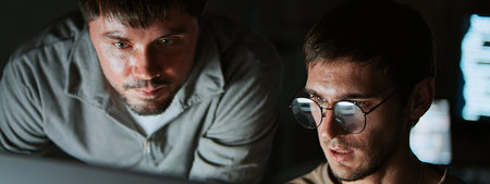 Two white Caucasian male software developers work together on program coding in home office late at...