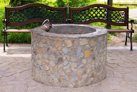 Decorative stone well with the figure of a pitcher is in a quiet alcove next to benches with curved wrought backの写真素材