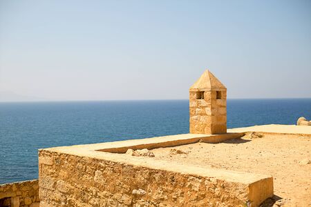 Walk along the old ruins of mediterranean coastal fort castle with a tower from pirimindalnoy roof high above the azure seaの写真素材
