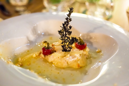 Delicious aromatic soft cheese marinated with a sprig of rosemary and pepper on a white figured plateの写真素材