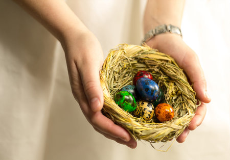 straw nest with eggs painted in different colors lie in the palm of the hand