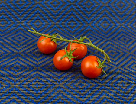 Bright fresh tomatoes on a branch lay on a blue textile backgroundの写真素材