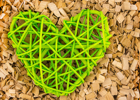 green wicker heart symbol of love of family loyalty against the background of a piece of wood chips close -upの写真素材