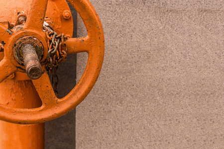 vertical pipe painted bright orange paint with big valve with chain mounted on the base closeup copy...