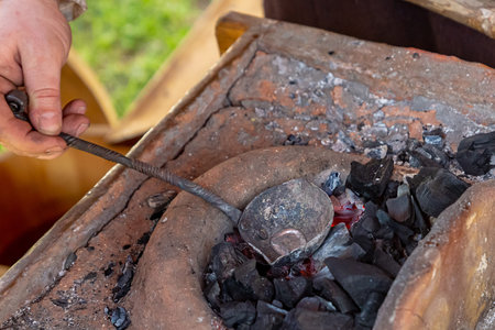 traditional production of blacksmith's work liquid silver metal melts in a leather black spoon on...