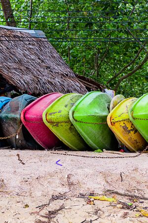 fishing boats are bright green, pink and yellow lying on a sandy tropical beach against the backdrop of a hut and forestの写真素材
