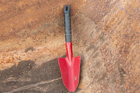 iron scoop, a small red shovel stands against a rusty and iron bucketの写真素材