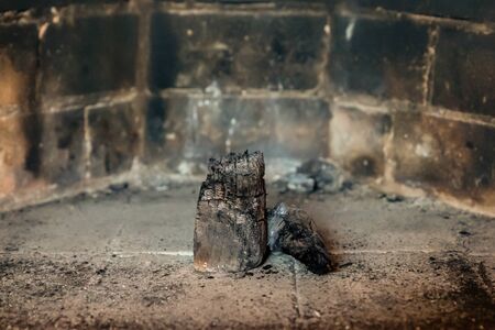 handful of black coals lay in the center of the fireplace, fuel leftovers against a smoked wallの写真素材