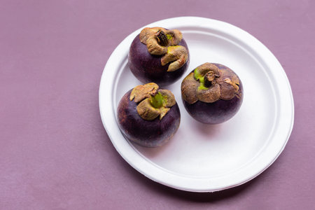 three mangosteen round tropical fruit lies on a white plate