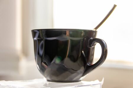 black glass cup with spoon close-up on a blurred window backgroundの写真素材