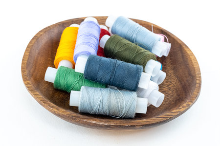 set of multi-colored sewing threads gray and blue folded in a wooden plate on an isolated background