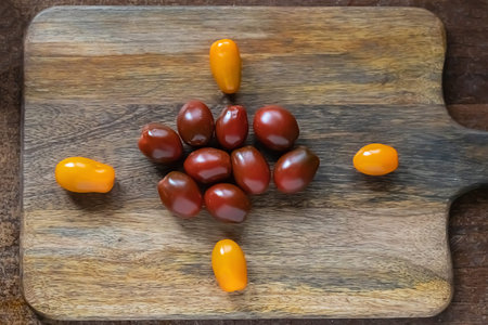black tomatoes in the center of the frame from yellow cherry tomatoes on a wooden backgroundの写真素材