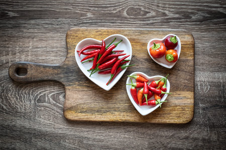 red chili pepper fresh on a white plate in the form of a heart on a dark wooden background