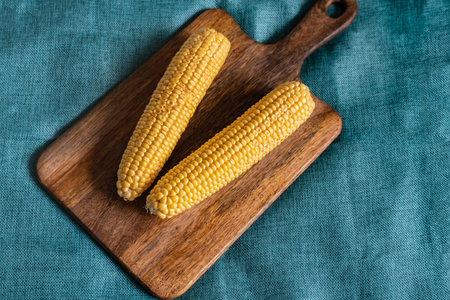 corn a couple of ripe cobs on a wooden cutting board dark brown backgroundの写真素材