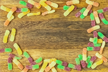 frame from gummy candies of worms on a wooden base, the basis for designの写真素材
