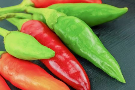 green and red chili peppers lie on a black background, small pods