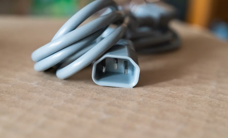 Electrical cable with three-prong connector resting on a cardboard surface in a well-lit indoor spaceの写真素材