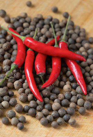 juicy hot spicy red chili peppers on wooden surface with peppercorns background