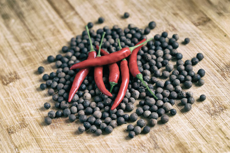 bright hot red chili peppers on a wooden surface surrounded by aromatic peppercornsの写真素材