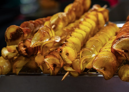 Delicious potato skewers topped with spices served at a street food market during evening hoursの写真素材