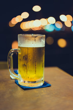 A glass of beer with bokeh light background on the bar.の写真素材