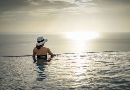 Women relax pool villa, infinity sea view, and a beautiful sunset.の写真素材