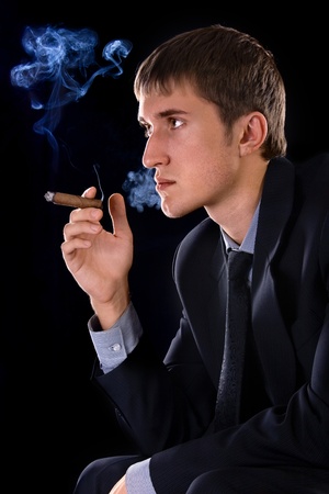 young smoking man with cigar on black backgroundの写真素材