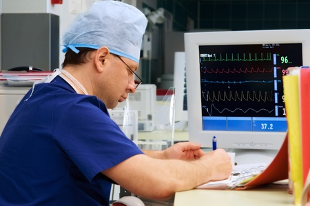 doctor in ICU writing prescription with monitorの写真素材