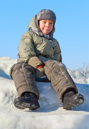 smiley boy sitting at snow with warm coatの写真素材