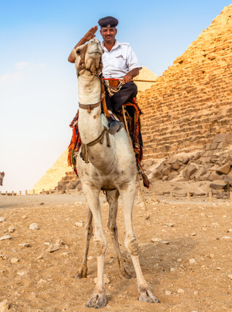 EGYPT, GIZA - OCTOBER 29 2014: A Man in Police Uniform Riding a Camel near the Giza Pyramidsのeditorial素材