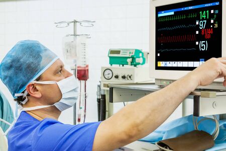 Experienced male anaesthesiologist at monitor in operation room