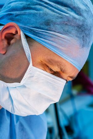 Close-up of male surgeon wearing surgical mask and cap performing an operation. の写真素材