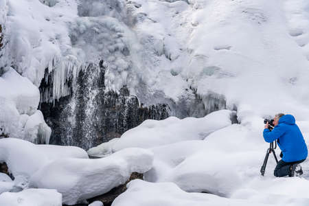 Photoghaper taking a photo at frozen waterfall in winterの写真素材