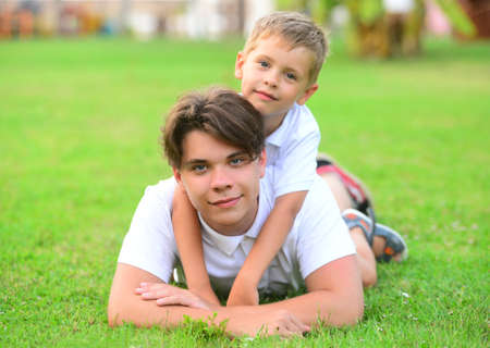 Older and younger brothers lying on green grass in park.の写真素材