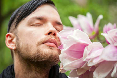 Portrait of young beautiful fashionable man in the flowered gardenの写真素材