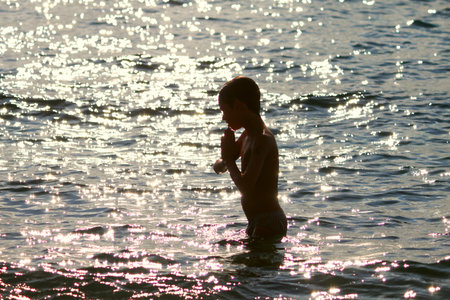 Silhouette of boy jumping in sea at sunsetの写真素材