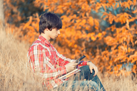 Young student working in autumn city parkの写真素材