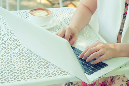 Woman drinking coffee and using a laptop on a white table.の写真素材