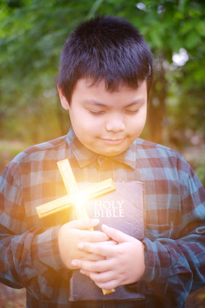 Christian boy  prayer to God. The Bible and the cross are in hand.