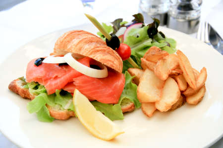 Big half moon stuffed croissant sandwich with smoked salmon, salad and home-cut friesの写真素材