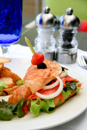 Big half moon stuffed croissant sandwich with smoked salmon, salad and home-cut fries.の写真素材